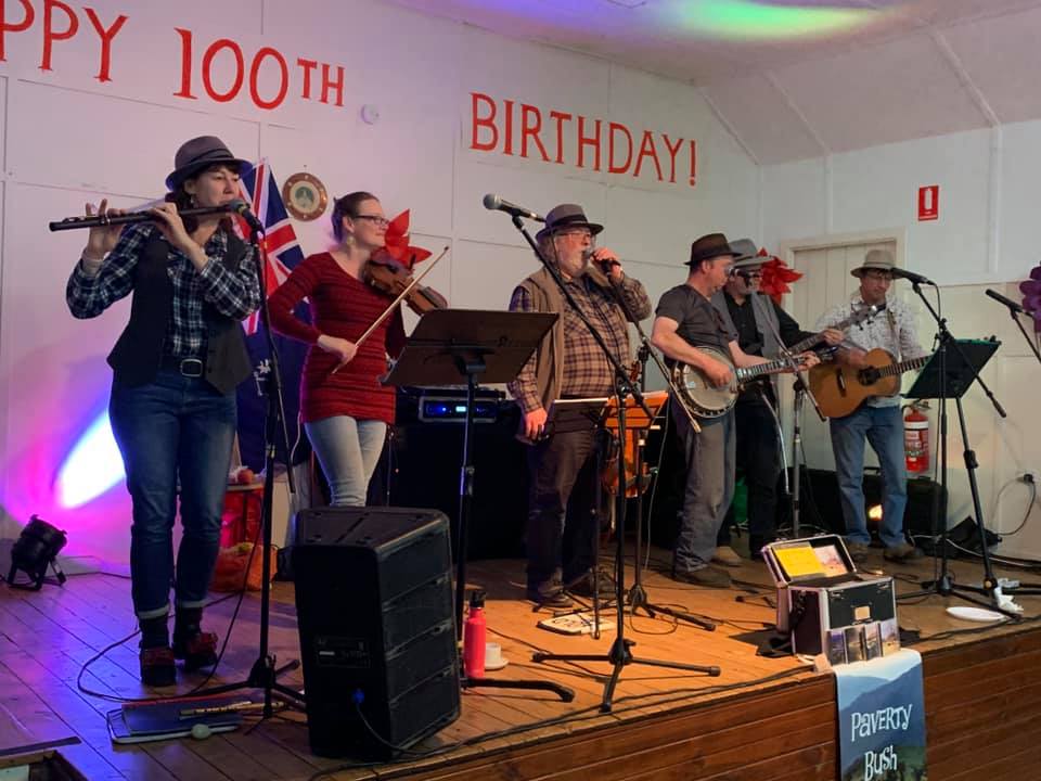 six members of Paverty Bush Band on stage - sign on the back wall says Happy 100th Birthday
